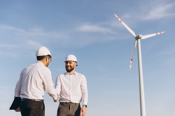 Engineers shaking hands in front of wind turbine