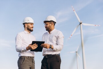 Engineers discussing next to wind turbines under blue sky