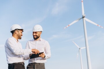Engineers using tablet next to wind turbines discussing about sustainable energy
