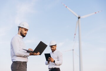 Engineers working with laptop and tablet near wind turbines