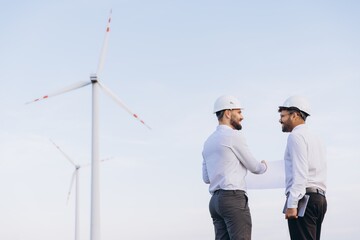 Engineers discussing blueprint in front of wind turbines