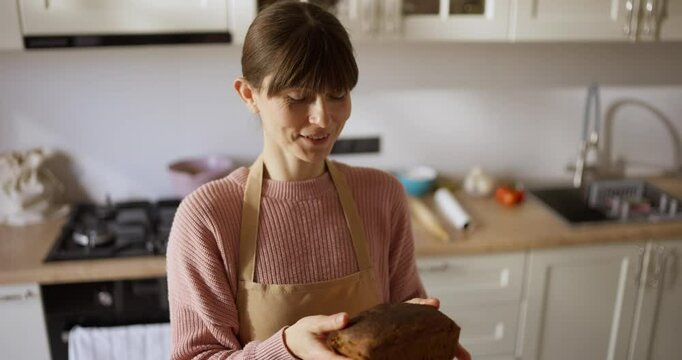 Woman smelling bread and smiling after cooking it in her modern kitchen at home. Happy woman baker amateur at home
