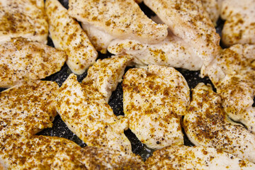 Raw chicken fillets seasoned with spices are arranged on a grill pan, showcasing the preparation...