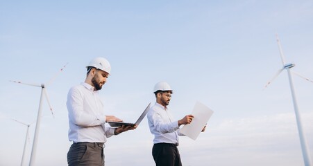 Engineers working on a wind turbine project using a laptop and blueprints