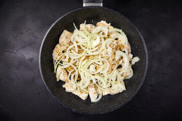 Sauteed chicken pieces with sliced onions and spices in a non-stick frying pan, showcasing vibrant textures and colors in a culinary preparation scene