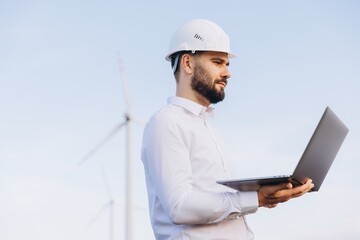 Engineer holding laptop inspecting wind turbines in field