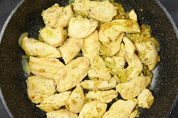 Sliced chicken breast pieces seasoned and sauteed with onions in a non-stick frying pan, showcasing a delicious cooking process and vibrant textures of the meal preparation