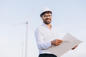 Arabian engineer examining blueprints at wind turbine farm for sustainable energy