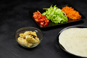 Fresh ingredients for a delicious wrap, featuring marinated chicken pieces in a bowl, vibrant...
