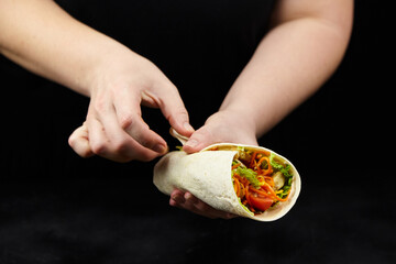 Hands of a person holding a fresh tortilla wrap filled with colorful vegetables, showcasing the...