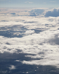 Expansive view of fluffy white clouds covering the sky, with soft sunlight filtering through,...