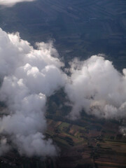 Fototapeta premium Aerial view of fluffy white clouds floating above lush green fields and agricultural land, showcasing the beauty of nature and the vastness of the landscape below