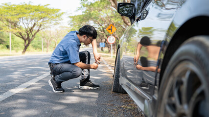 Mechanic or driver providing roadside assistance by changing a flat tire and performing minor...