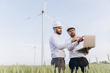 Engineers inspecting wind turbines with a laptop in a wheat field