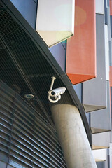 White security camera mounted under an architectural overhang with black mesh ceiling and concrete...