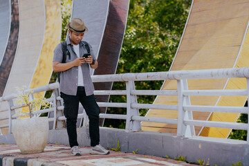 Full length of Asian man traveler using a mobile phone on the road city street. Enjoying road trip. Backpacker and travel lifestyle.