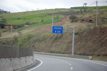 Sinalização rodoviária indicando pedágio a 1 km com opção de cobrança automática à direita. Foto ideal para temas de mobilidade, transporte rodoviário e infraestrutura no Brasil.