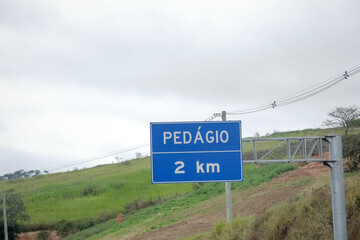 Sinalização rodoviária indicando pedágio a 1 km com opção de cobrança automática à direita. Foto ideal para temas de mobilidade, transporte rodoviário e infraestrutura no Brasil.