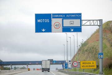 Sinalização rodoviária indicando pedágio a 1 km com opção de cobrança automática à direita. Foto ideal para temas de mobilidade, transporte rodoviário e infraestrutura no Brasil.