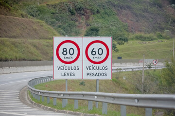 Sinalização rodoviária com limites de velocidade distintos para veículos leves (80 km/h) e pesados (60 km/h), em estrada brasileira. Ideal para temas de trânsito, segurança viária e transporte.