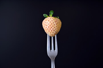 pineberry on a fork on a black background close-up, copy space