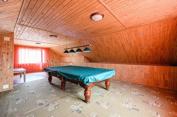 Wooden attic game room features a covered billiard table, carpeted floor, paneled walls, and...
