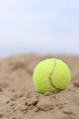 Yellow tennis ball lies on the sand. Sports and recreation concept, summer games. Tennis or paddleball ball. Tennis court near the beach. Paddleball ball on the sand near the water. Outdoor games