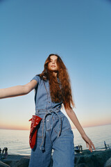 Lifestyle woman in modern boho-western denim street style with long hair by the sea during golden...
