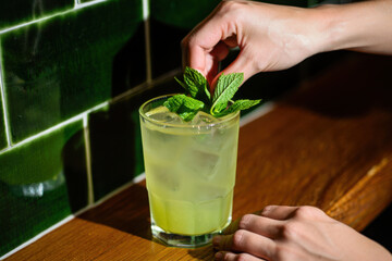 Bartender adding fresh mint leaves to green cocktail