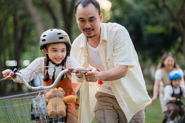 A man is helping a child ride a bike. The child is wearing a helmet. The man is holding onto the...