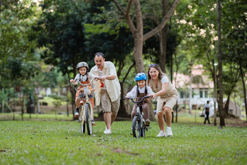 A family of four riding bikes in a park. A man is riding a bike with a child on it