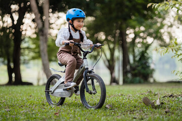 A young girl is riding a bicycle in a park. She is wearing a helmet and a white shirt