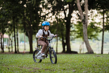 Fototapeta premium A young girl is riding a bicycle in a park. She is wearing a helmet and a white shirt