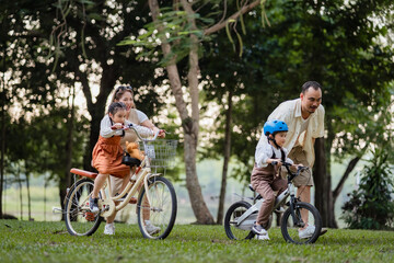 A family of four riding bikes in a park. A man is helping a child on a bike