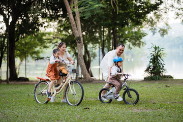 A family of four riding bikes in a park. A man is riding a bike with a child on it