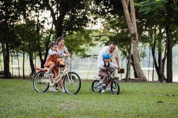 A family of four riding bikes in a park. A man is riding a bike with a child on it