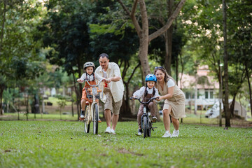 A family of four riding bikes in a park. A man is riding a bike with a child on it
