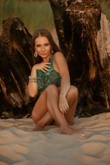 Naklejka premium A woman in a green palm-print bikini, adorned with jewelry, gazes softly into the distance, illuminated by the warm glow of the setting sun