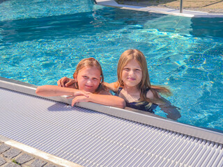 Two cheerful girls delightfully enjoying a refreshing swim in a pool on a bright, sunny day