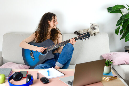 A Young Woman Enjoying Playing Guitar Alongside Her Cat in a Cozy Home Office Space