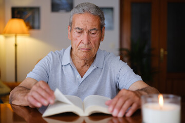 Elderly man flipping a book page by candlelight in his living room.