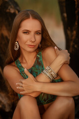 A woman in a green palm-print bikini, adorned with jewelry, gazes softly into the distance,...