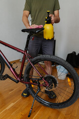 Vertical shot of cyclist male cleaning saddle of mountain bike using spray bottle and cloth,...