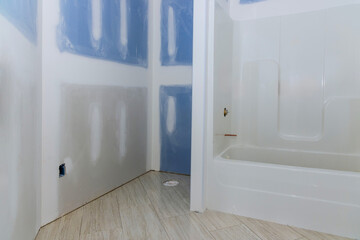 Newly installed bathtub in bathroom during renovation with unfinished drywall floor tiles.