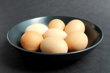 On a black background, there are chicken eggs in a black plate.