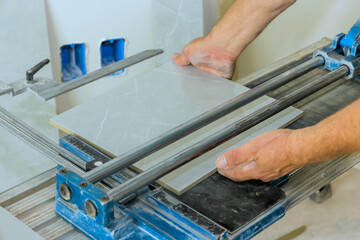 Skilled worker uses tile cutter to carefully slice a large ceramic tile at construction site.