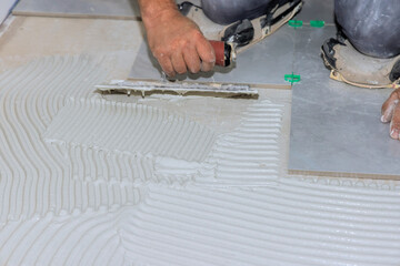 Worker skillfully spreads tile adhesive on floor surface for home renovation project.