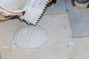 Worker spreads drying mortar on floor in preparation for tile installation in newly renovated space.