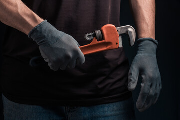 Plumber holds wrench in his hands with gloves on black background.