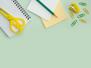 Notebook, paper clips, scissors and stapler on a light green background, top view. Space for text